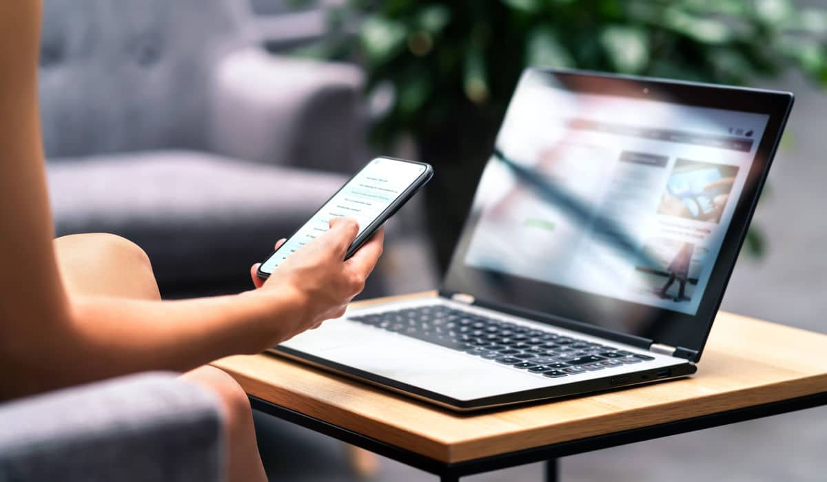 E-Commerce-Fulfillment Service Person sitzt von einem Laptop und hat ein Smartphone in der Hand